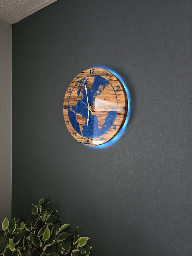 Spalted beech world map wall clock with deep blue resin oceans and integrated LED halo backlight, 315mm handmade wooden clock by The Humble Woodshed.
