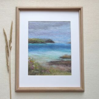 Waves of crystal blue sea lap the shoreline, headland in distance and wildflowers growing on the edge of the beach.