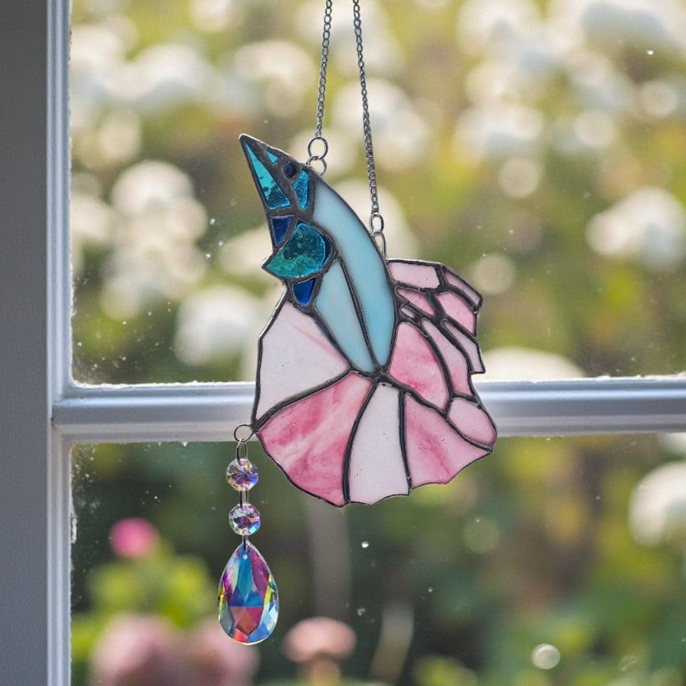 Pastel pink and blue glass fish suncatcher hanging in a sunny window, showing rainbow reflections from the crystal prism