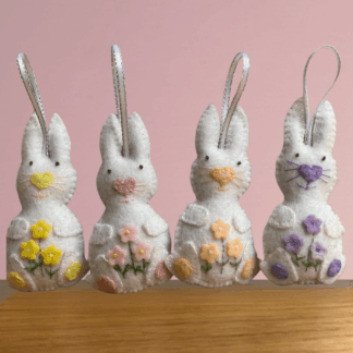 Four handmade white easter bunny decorations each one carrying pretty felt flowers, the bunnies have a large pom pom tail