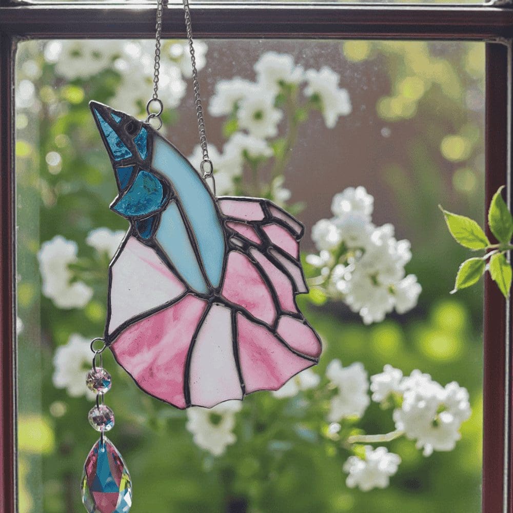 Close-up of pink and blue stained glass fish suncatcher catching sunlight and creating colourful rainbows from the attached prism