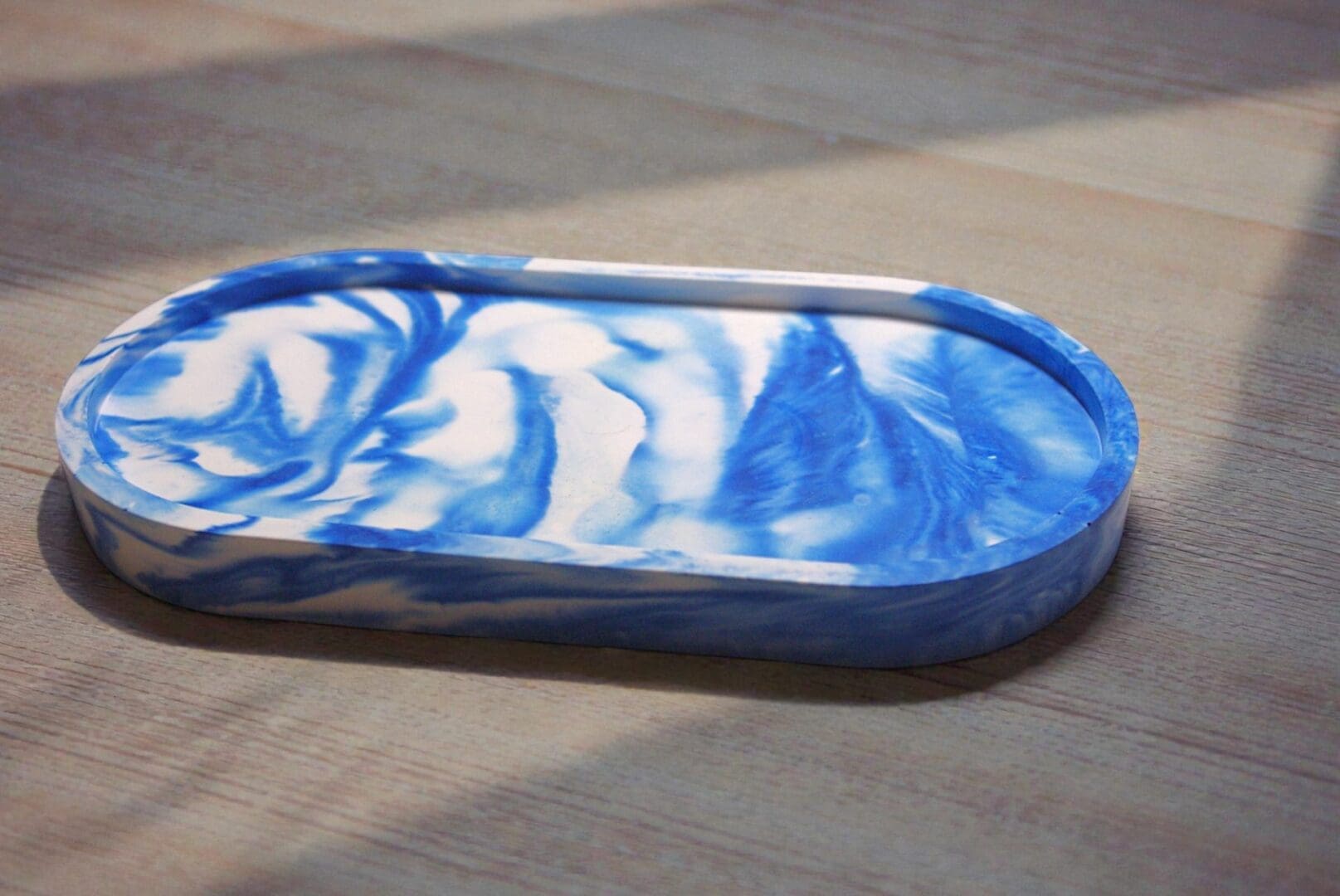 A blue and white oval trinket tray is on a pale wooden countertop in a patch of sunlight.