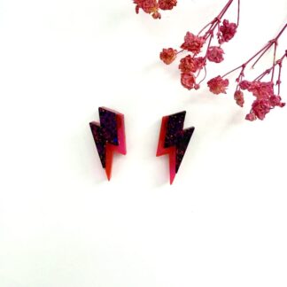 Bold neon pink and black glitter lightning bolt earrings with surgical steel posts displayed on a white background with pink flowers