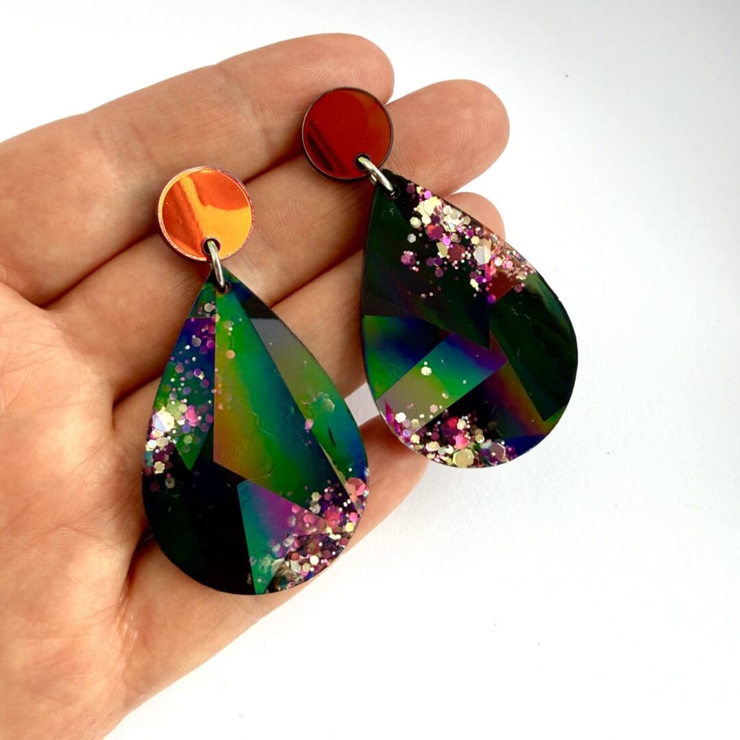 Black holographic teardrop earrings hung on mirrored acrylic stud toppers with surgical steel posts and backs, shown on a hand for size.