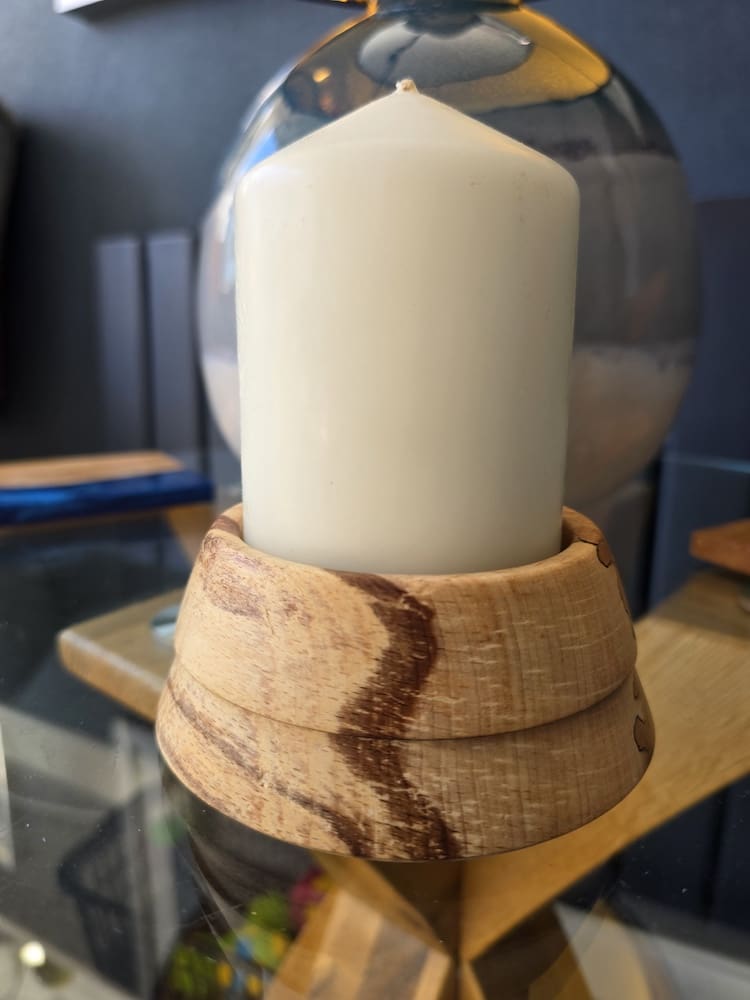 Flaming beech wooden candle holder with unique grain patterns and white pillar candle on glass surface