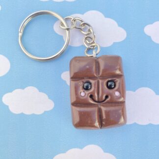 Handmade polymer clay chocolate bar keyring. Made using a dark chocolate colour with the classic indents for the squares of chocolate and a kawaii style smiling face. Glass black bead eyes, smiling face and rosy cheeks.