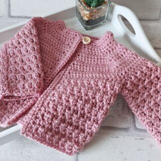 A handmade pale rose crochet baby cardigan featuring a textured cluster stitch pattern and a relaxed fit.