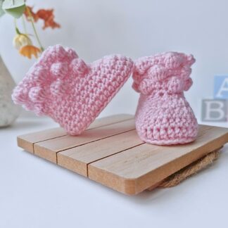 Pair of handmade crochet baby booties featuring a textured bobble-stitch cuff in powder pink on a neutral background.
