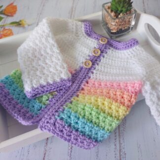 A white handmade crochet baby cardigan with a textured stitch and soft pastel rainbow stripes around the bottom edge.