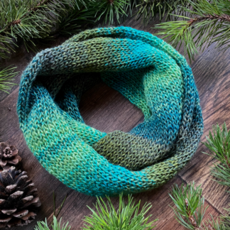 Green rainbow knitted cowl scarf laying encircled in fir boughs