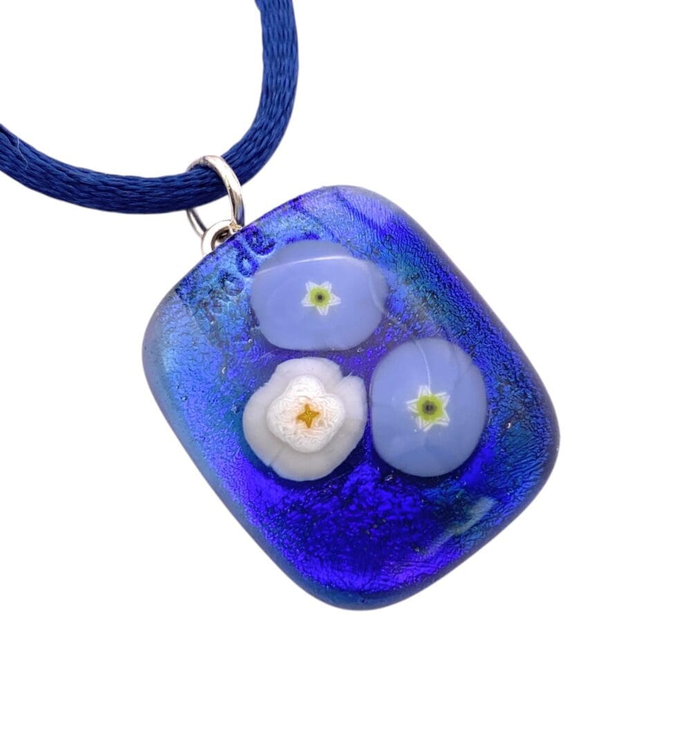 Blue glass pendant with embedded white and light blue flower designs on a blue cord necklace.