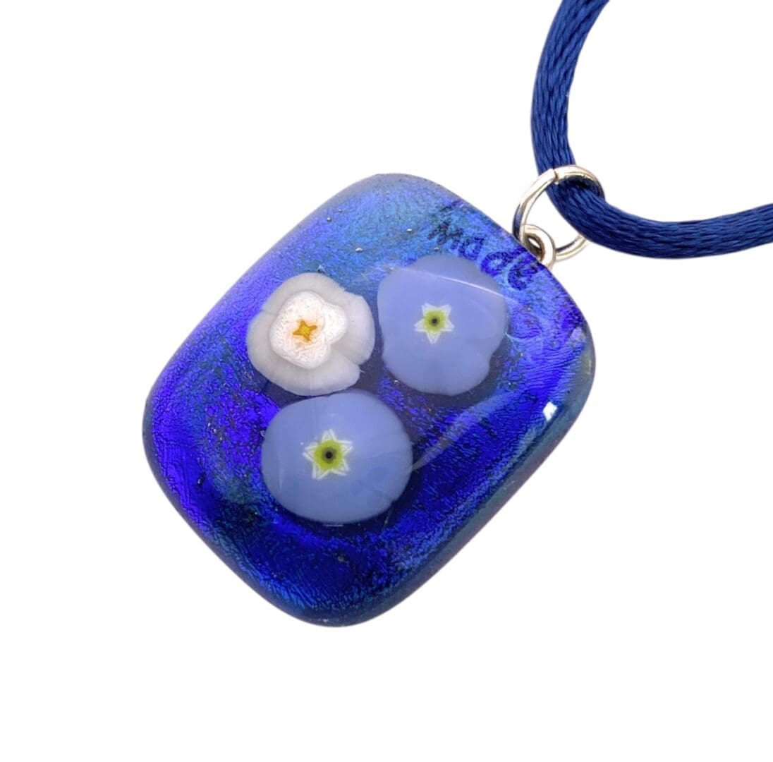 Rectangular blue glass pendant with embedded white and light blue floral designs, attached to a blue fabric cord necklace.