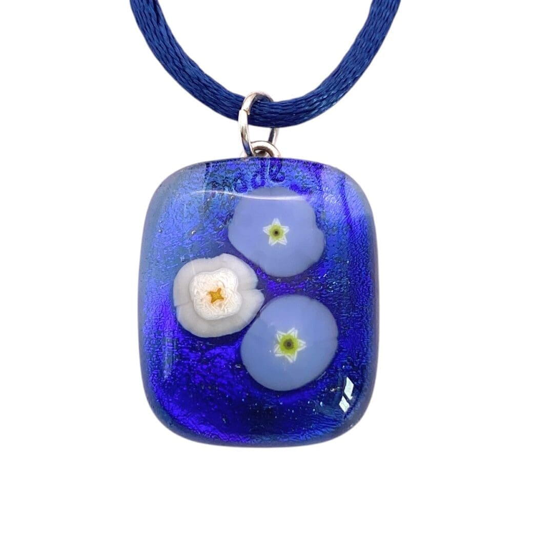 Blue glass pendant with three delicate white and light blue floral designs on a blue cord necklace.