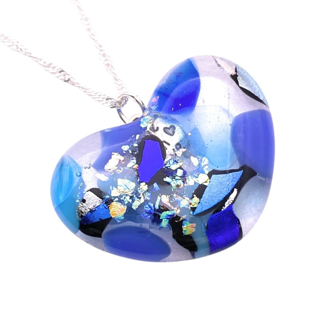 Heart-shaped glass pendant necklace with blue, black, and iridescent patterns on a silver chain, photographed on white background.