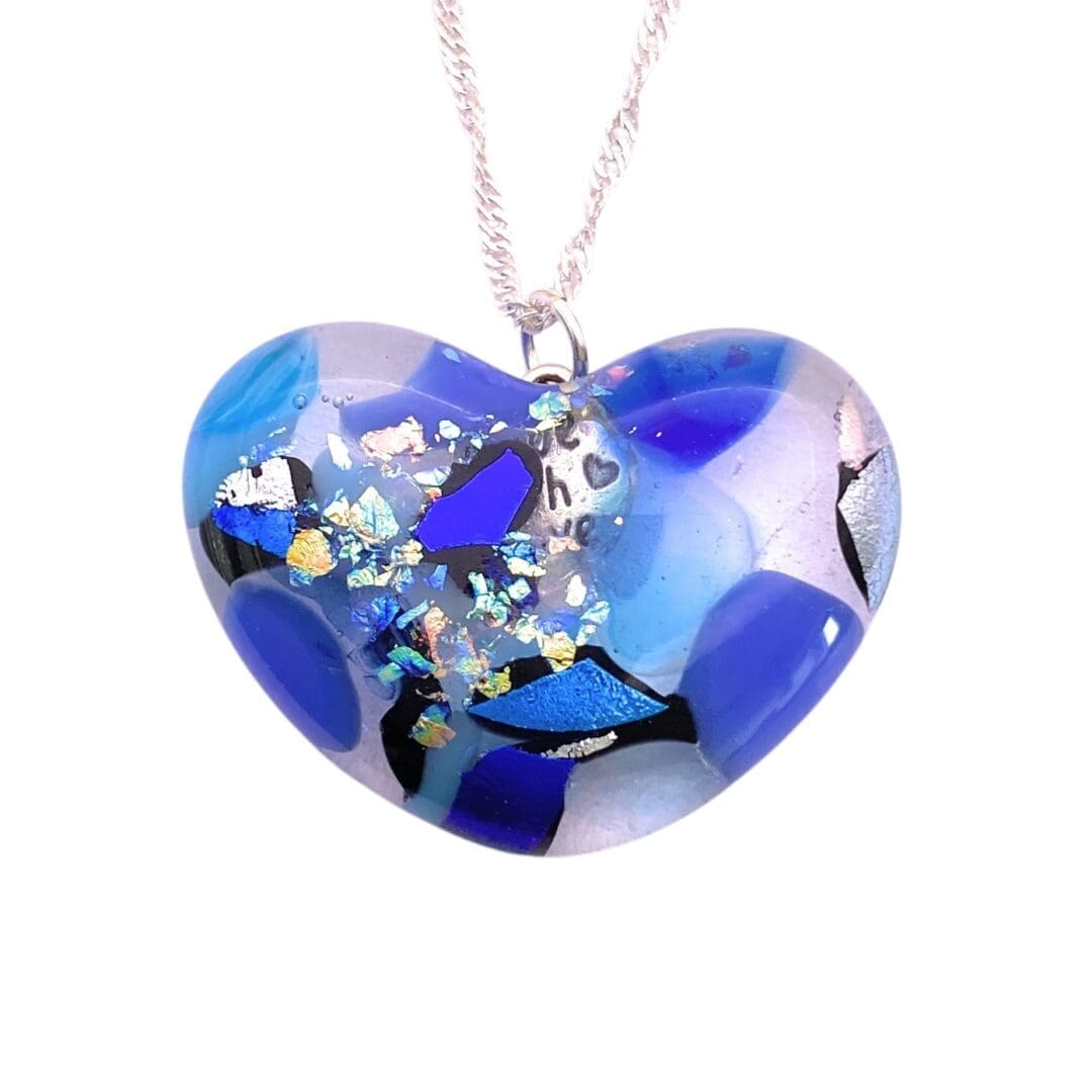 Heart-shaped glass pendant with blue, black, and iridescent shards, creating a mosaic effect. Set on a twisted silver chain; artistic and elegant design.