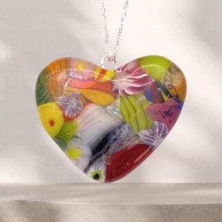 A heart-shaped glass pendant features vibrant, embedded flowers and patterns in yellow, pink, green, and orange, hanging on a delicate chain.