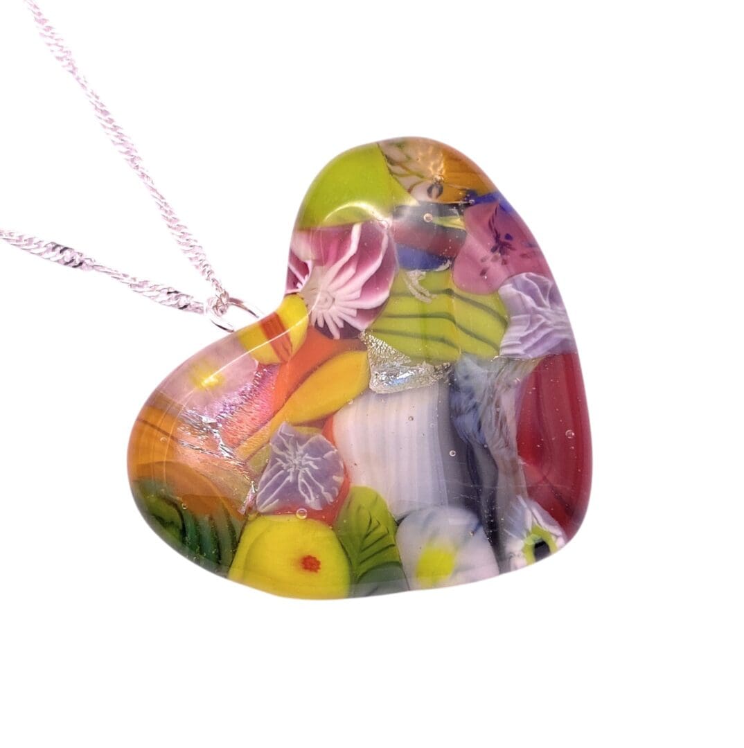 Heart-shaped pendant with colorful floral patterns encased in clear glass, on a delicate chain. The design conveys a vibrant, cheerful tone.