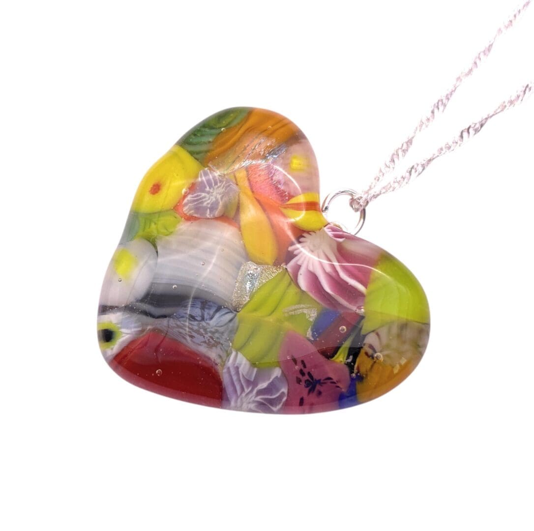 Heart-shaped glass pendant with vibrant floral designs, featuring pink, yellow, and green hues. The pendant hangs from a delicate silver chain.