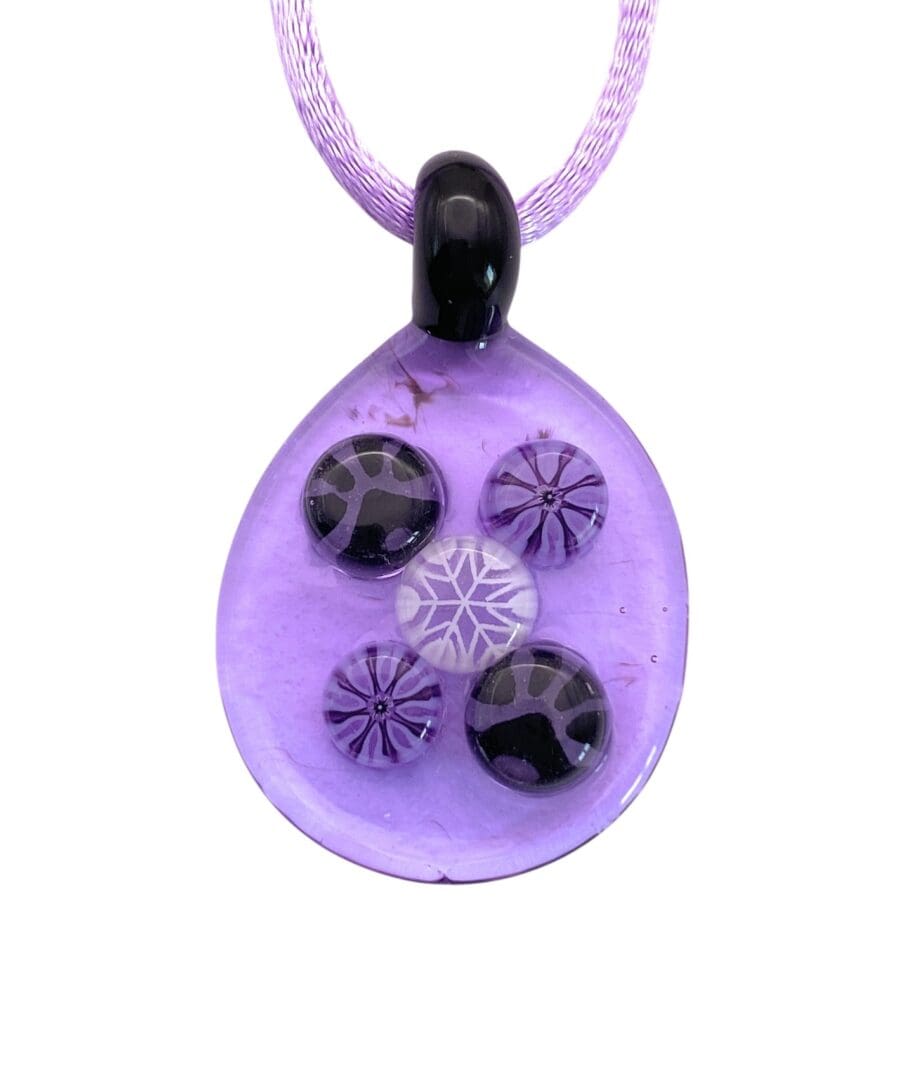 A purple glass teardrop pendant with five decorative circular designs, featuring a mix of purple and black paw print colors, strung on a lavender cord.
