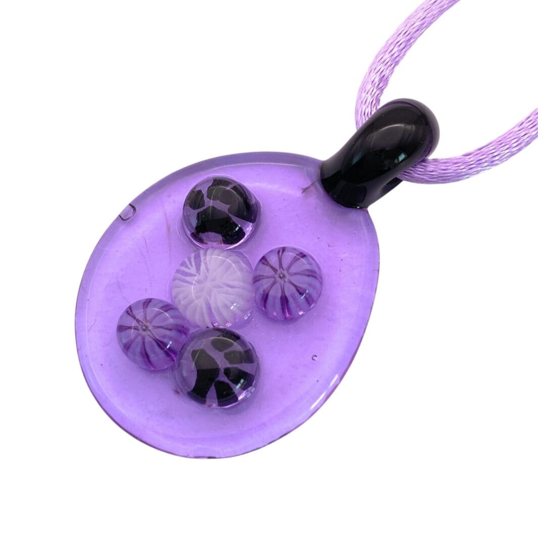 Purple glass pendant with a black top, featuring embedded colorful spheres. Hangs on a purple cord, conveying a playful and artistic tone.