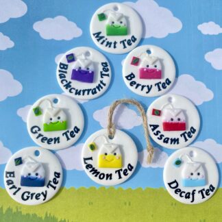 A variety of eight kitchen labels, on a white circle base, each one has a kawaii style tead bag featuring corresponding colours and the name of the tea, Which include - yellow - lemon tea, pink - berry tea, purple - blackcurrant tea.
