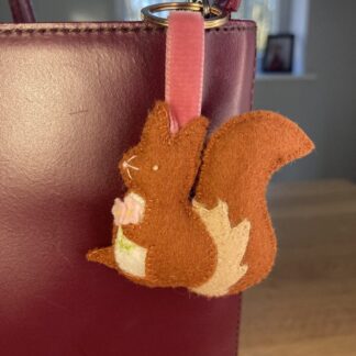 Squirrel bag charm shown on a maroon handbag