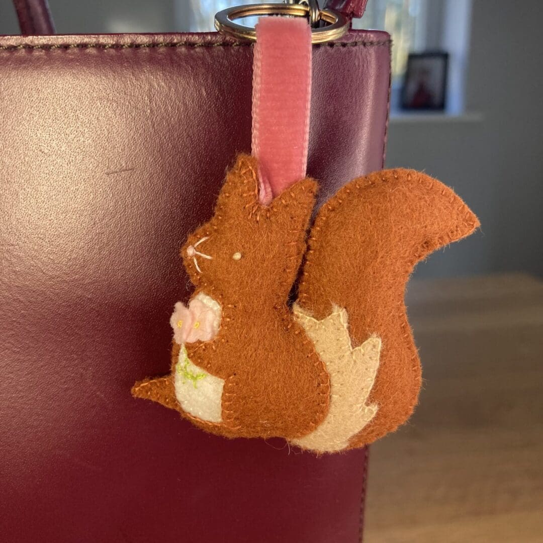 Squirrel bag charm shown on a maroon handbag