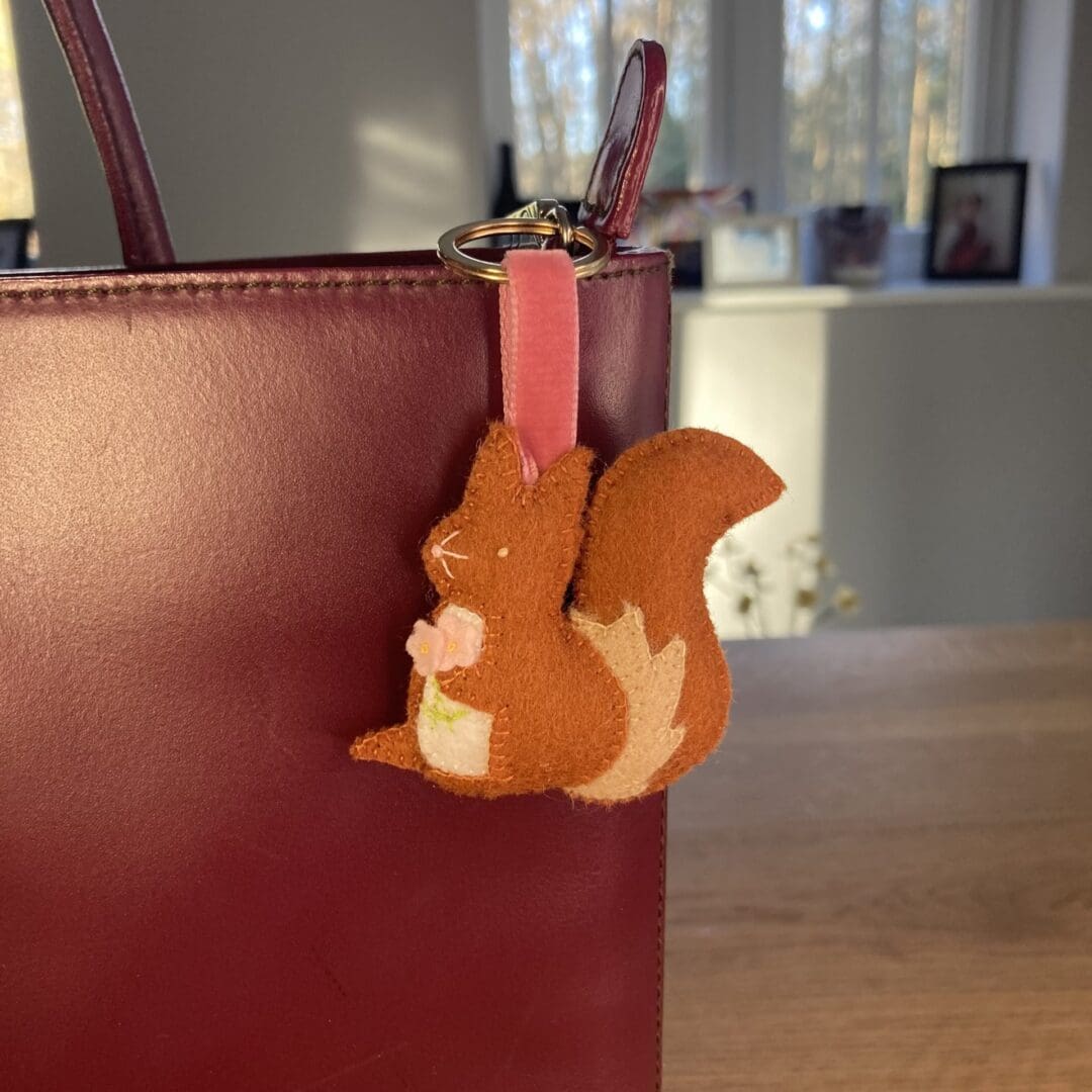 Handmade felt squirrel bag charm on a pale pink velvet ribbon attaching it to a rose gold slip ring