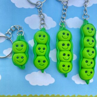 Four green pea pod keychains with smiling faces. The keychains are different sizes, with the largest keychain having five peas and the smallest keychain having two peas.