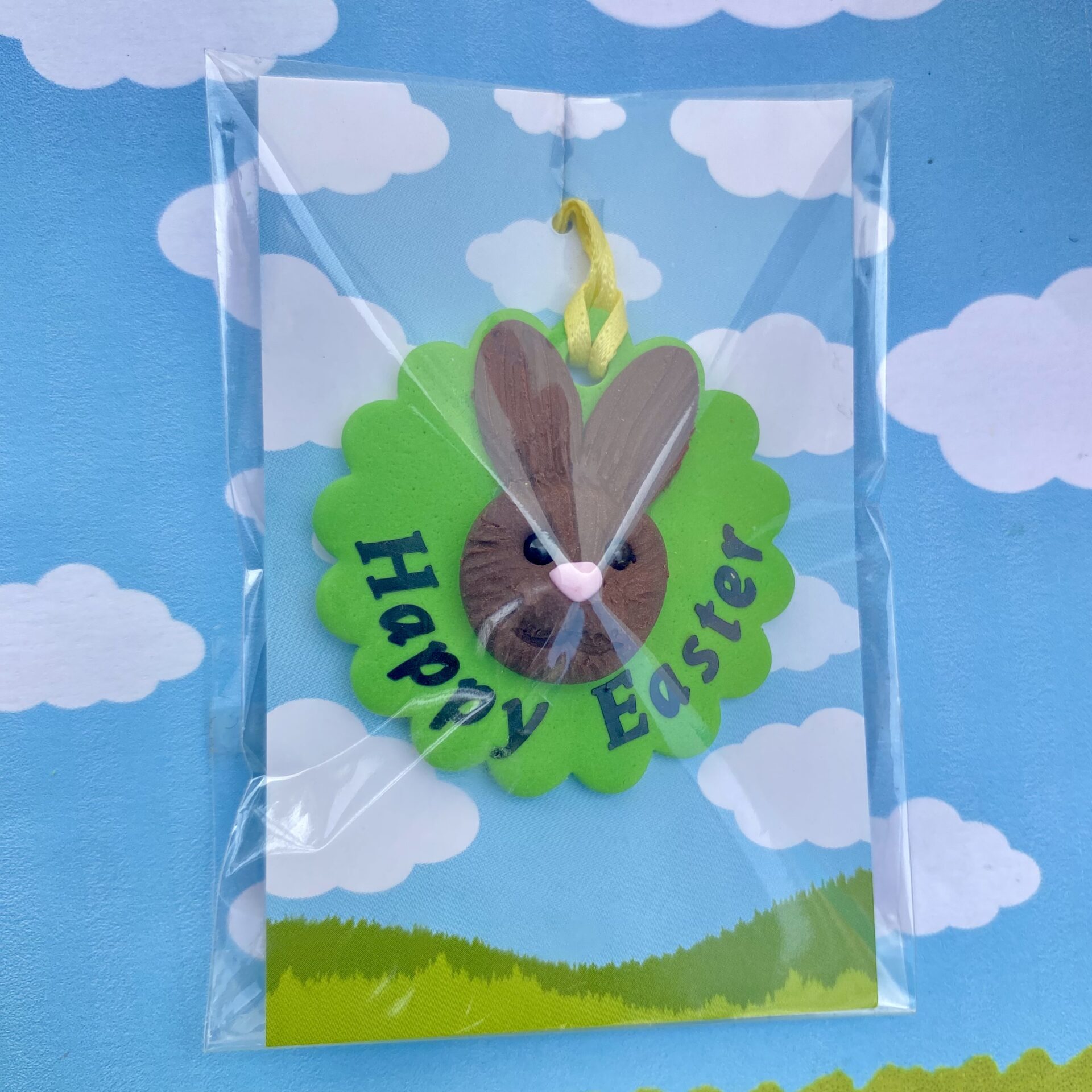Handmade polymer clay bunny rabbit tree decoration. Each bunny features a sculpted brown face with long upright ears, a pink nose, sparkling black bead eyes, and a cheerful smile, all set on a vibrant green base and finished with a sunny yellow ribbon for easy hanging. Includes the writing - happy easter 2026, to show the option of personalisation