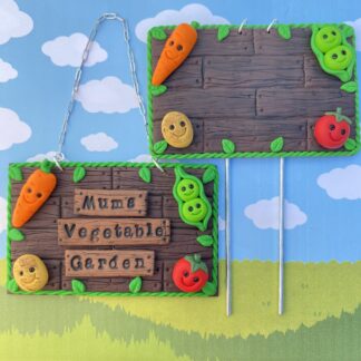 A handmade personalised polymer clay, brown wooden effect sign with a rustic wood grain texture. with a vine effect edge and smiling vegetables in the corners. Includes - carrot, peas, tomato & potato. The sign can be displayed using a hanging chain or a garden stake.