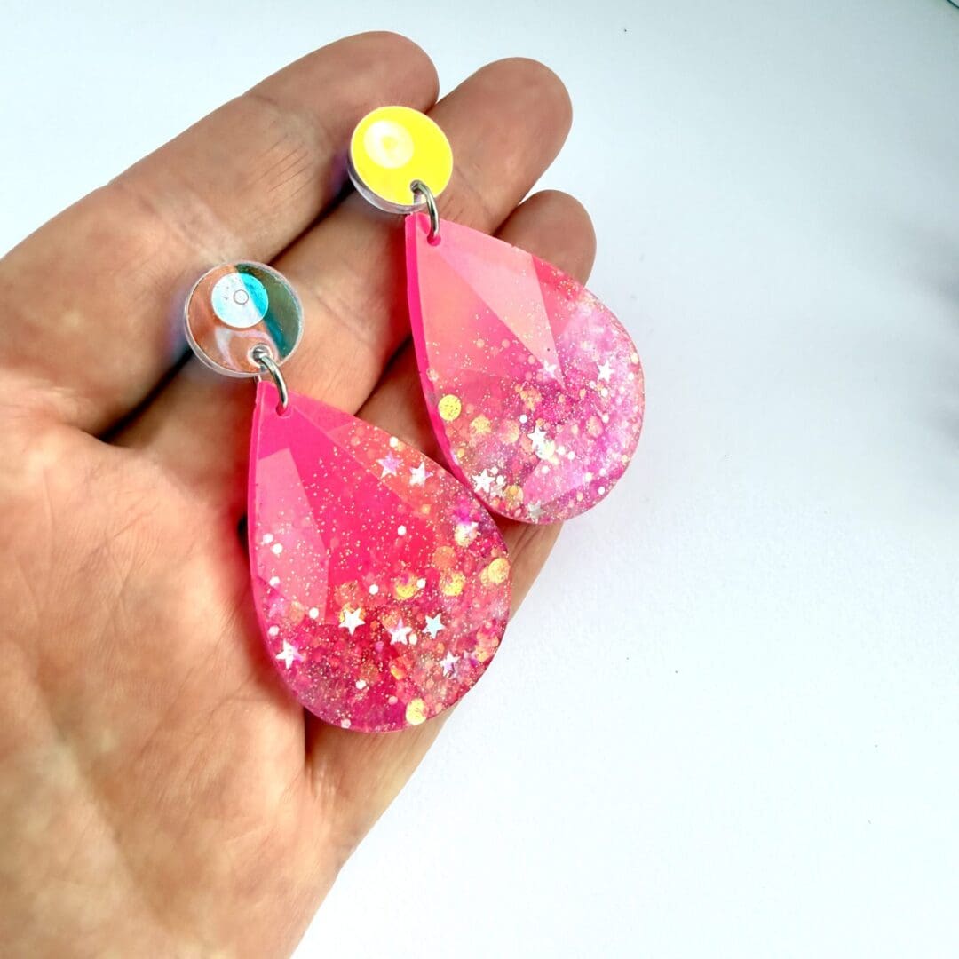 Pink holographic faceted teardrop resin statement earrings with glitter detail. Displayed on a hand for size.