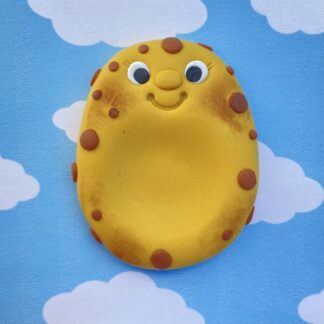 A smiling potato worry stone with brown spots and rosy cheeks against a blue sky with clouds.