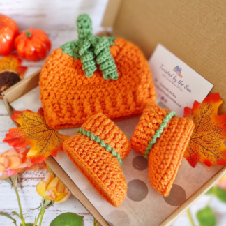 Handmade crochet pumpkin baby hat and booties set in orange and green, gift-boxed for a first Halloween present.