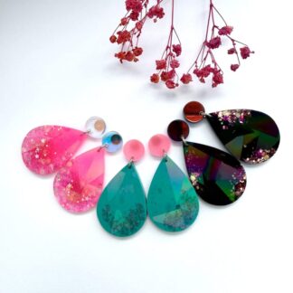 Pink, Teal and Black holographic hypoallergenic teardrop earrings shown side by side on a white background with pink flowers.