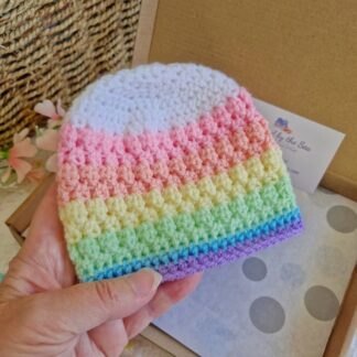 A white textured crochet baby hat with vibrant rainbow stripes down to the brim.