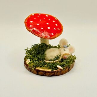White needle felt Mouse Sleeping Under Fly Agaric Mushroom made from clay, handpainted red with white spots. Mounted on wooden base, adorned with real green moss and white clay flowers.