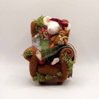 Needle felt, differently abled, white mouse wearing red bow by ear, green and maroon pajamas, with only one arm, cuddling a teddy bear in lighter brown with a yellow bow, lying asleep in an armchair of brown wool felt. Repurposed fabric draped on armchair with real moss accents.