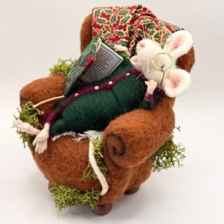 Needle felt white mouse wearing metal gold glasses and dark green felt pajamas with maroon trim, lying asleep in an armchair of brown wool felt, holding a dickensian novel bound in fabric. Repurposed fabric draped on armchair with real moss accents.