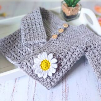 A silver handmade crochet baby cardigan with a textured V-stitch and a small yellow and white daisy attached to the front.