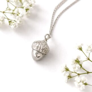 A small ackrn necklace in fine silver with a sterling silver chain. It is displayed on a white backgroun with some baby’s breath flowers.