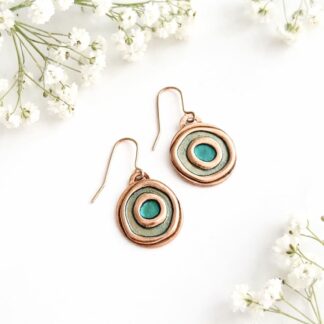 A pair of small round copper drop earrings with copper ear wires, the double circle design has been hand-painted, the outer circle is pale green metallic paint and the centre circle is kingfisher metallic paint. The earrings are displayed on a white background.