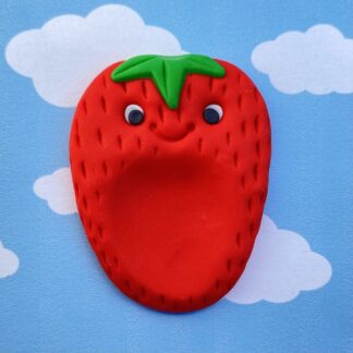 A cartoon strawberry worry stone with a smiling face and green leaves on a background of a blue sky with white clouds.