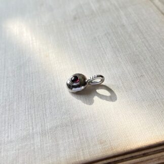 organic shaped oval pendant in silver, set with a round red garnet and a pendant loop with three notches.