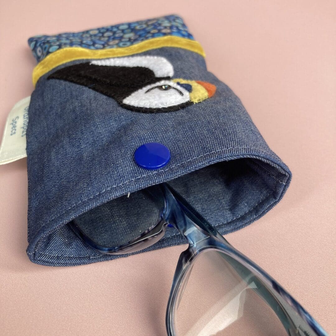 Glasses popping out of the puffin glasses case showing the inside of the case and the snap fastener to close the case.