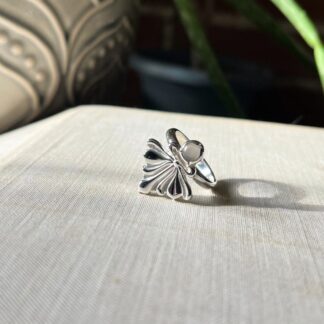 A silver ring with a lace style pattern and a round grey moonstone set beneath it.