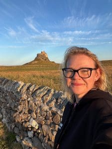 Susanne the shop owner standing in front of Lindisfarne Castle