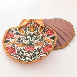 Arts and crafts inspired decoupaged scallop shell jewellery dish with flowers and bird design rests across the reverse of the same dish painted in a dusky pink.