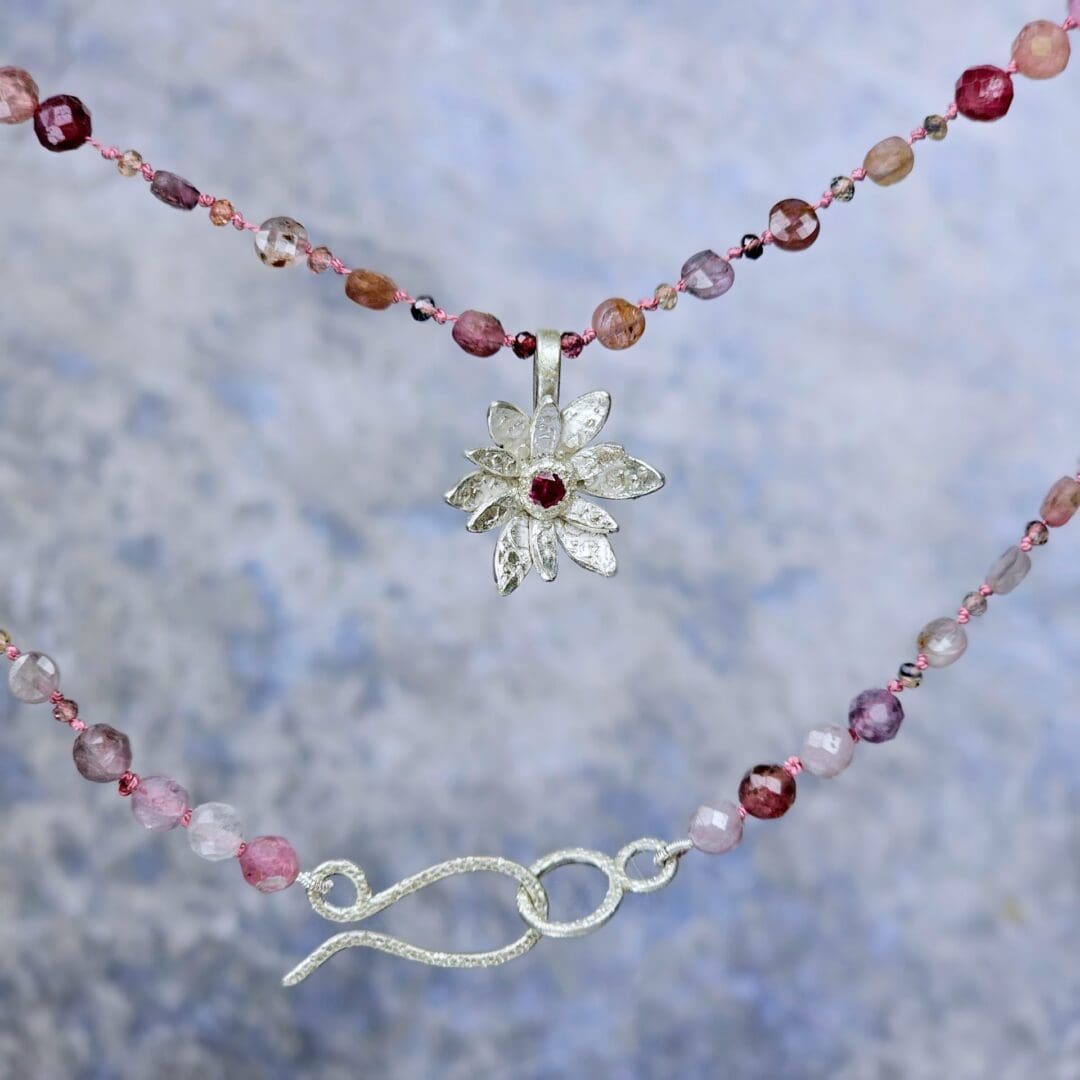 Spinel bead necklace with an etched silver flower pendant set with a small lab ruby at the centre, hanging, Isobel Kelly Jewellery