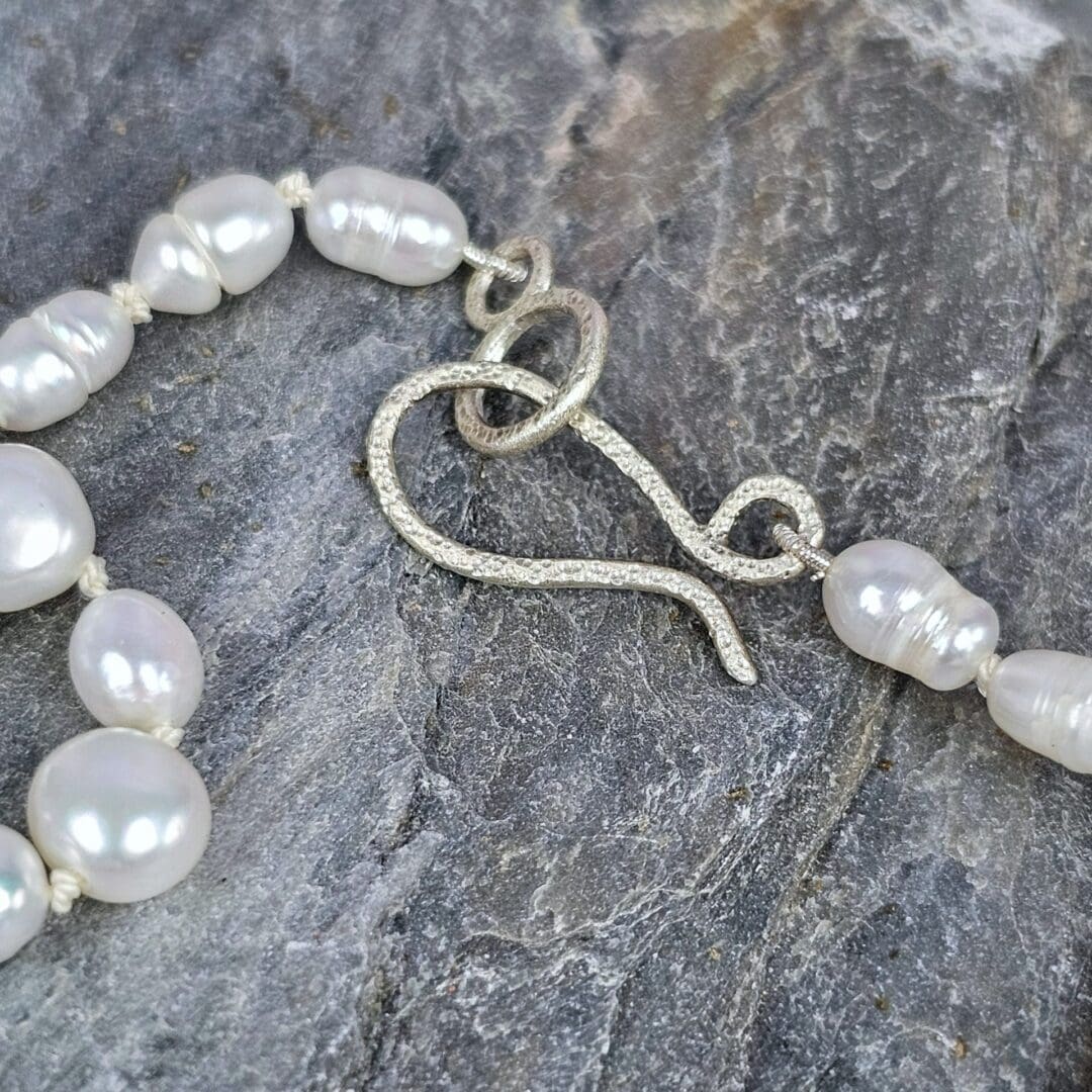 White baroque pearl necklace with a small etched silver heart pendant on a silk knotted strand, clasp on rock, Isobel Kelly Jewellery